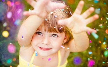 Portrait Of A Happy Little Girl Looking Up At Confetti Falling On Her